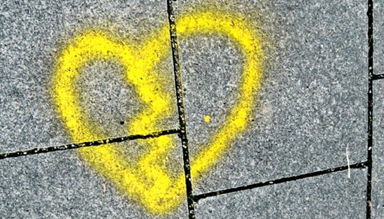 A spray-painted heart in yellow on the sidewalk with a jagged line through it