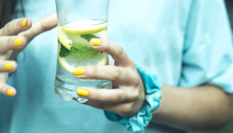 hands with colorful nails hold glass of water with lemon and mint