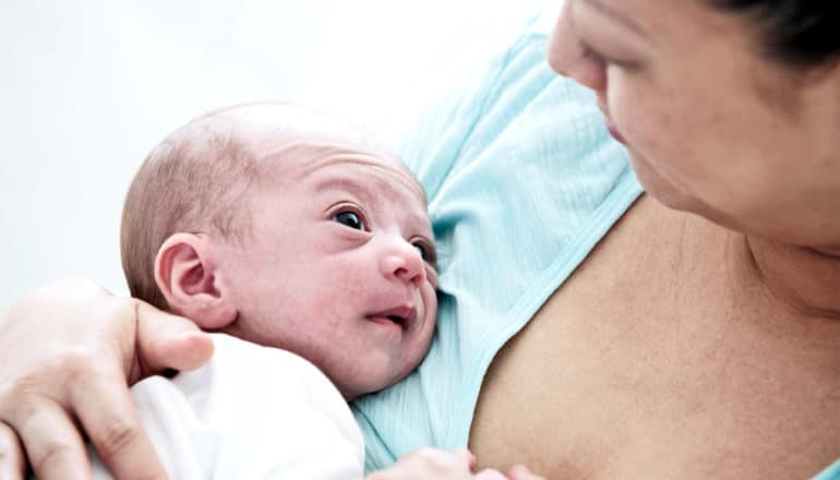 A mother holds her newborn as the baby looks up at her