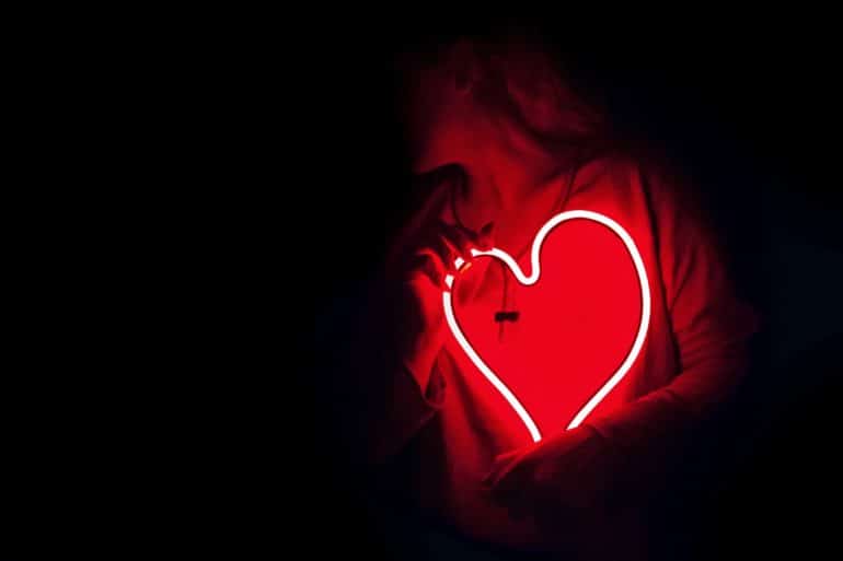 A person holds a neon light heart over their chest