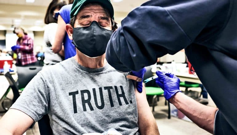 A man in a t-shirt that reads "Truth" gets a COVID-19 vaccine while closing his eyes