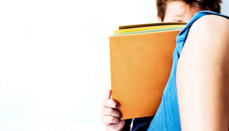 A young boy reads a book that's covering his face