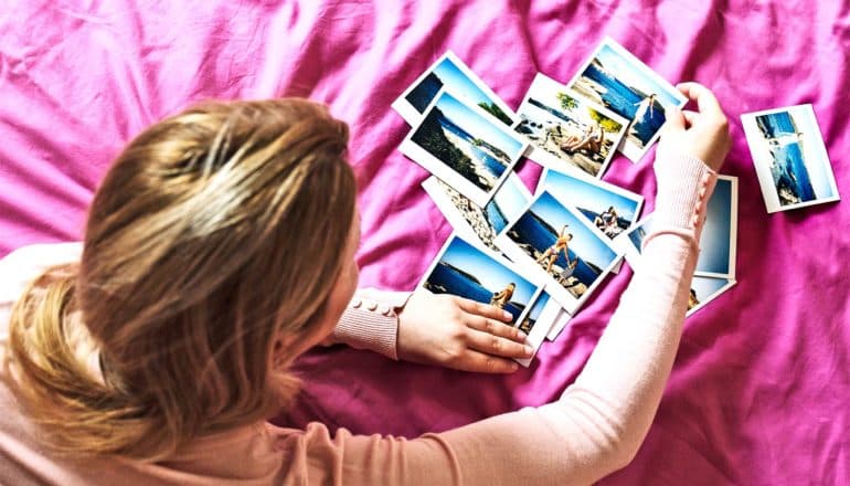 A woman on a pink sheet on a bed looks over photographs