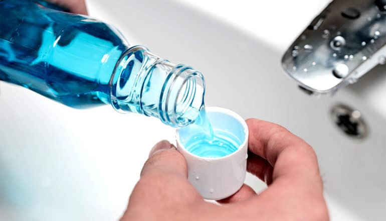 A person pours blue mouthwash into the container's cap