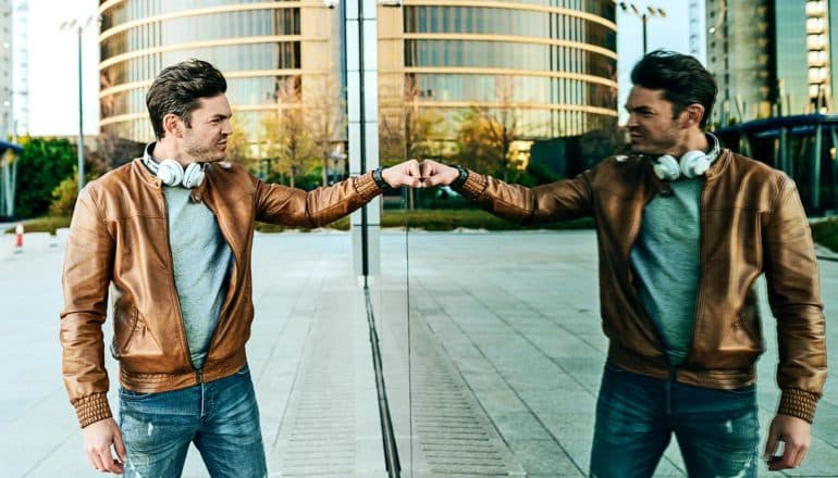 A man fist bumps his own reflection while walking past a large window