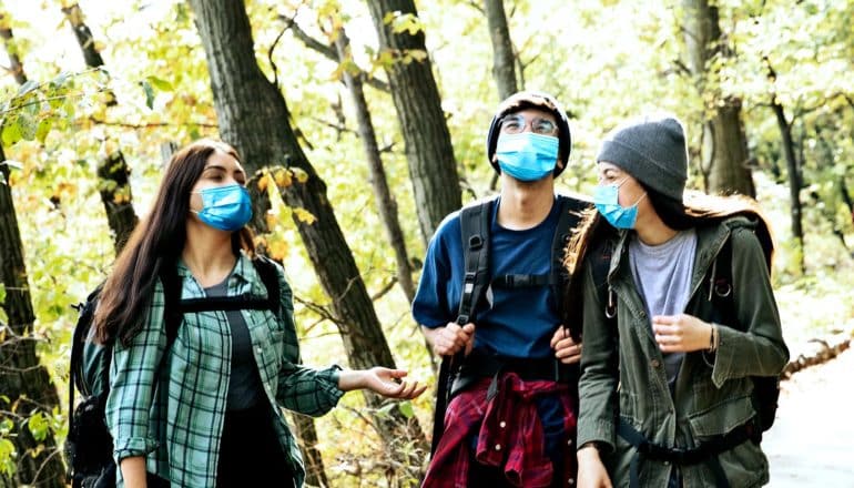 Teens walking along a forest path with backpacks and blue face masks on