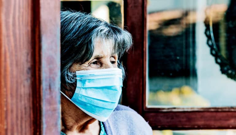 A nursing home resident looks out a door while wearing a face mask