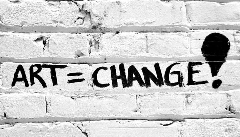 graffiti on brick wall says "art = change!"