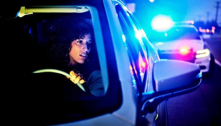 A woman looks in her rear view mirror as a police car flashes its lights from behind her