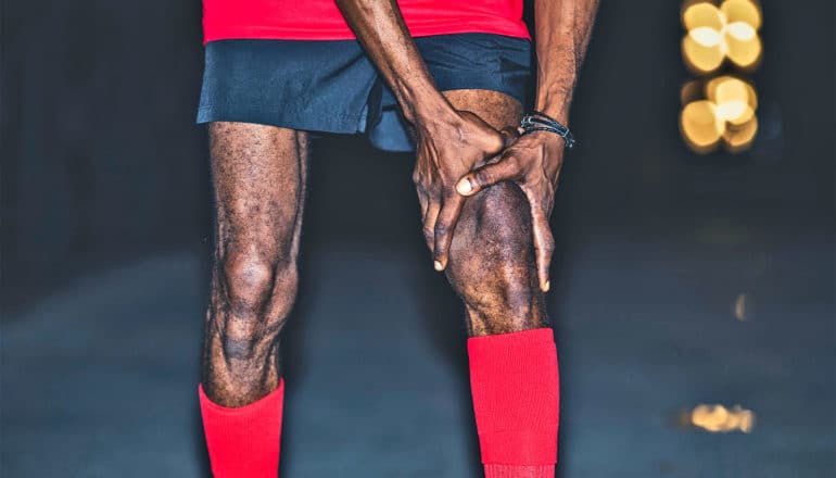 A runner grabs his knee while stopped on a road at night