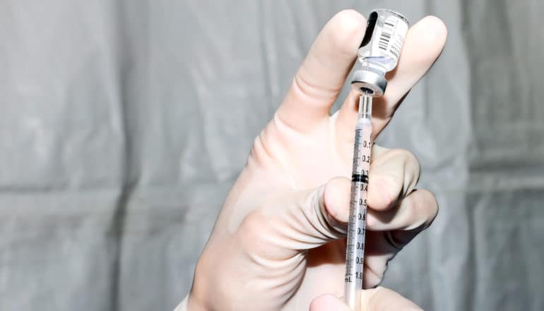 gloved hand fills syringe from vial