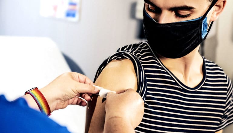 A health care worker puts a bandaid on a young man's arm over a vaccine injection site