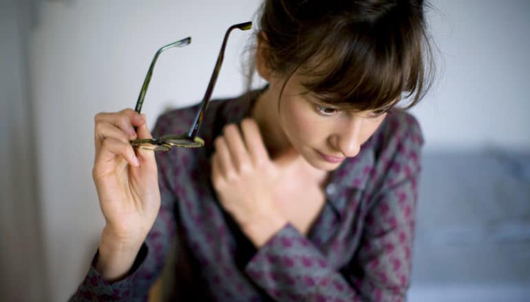 woman looks spaced-out while holding glasses off face