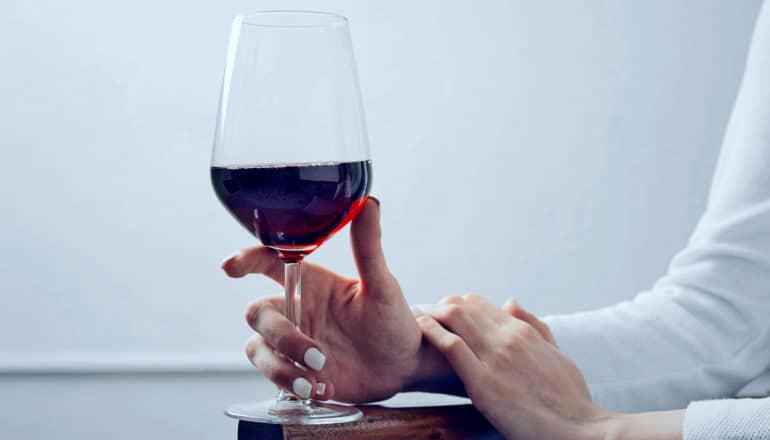 A woman holding a glass of wine on the arm of a chair