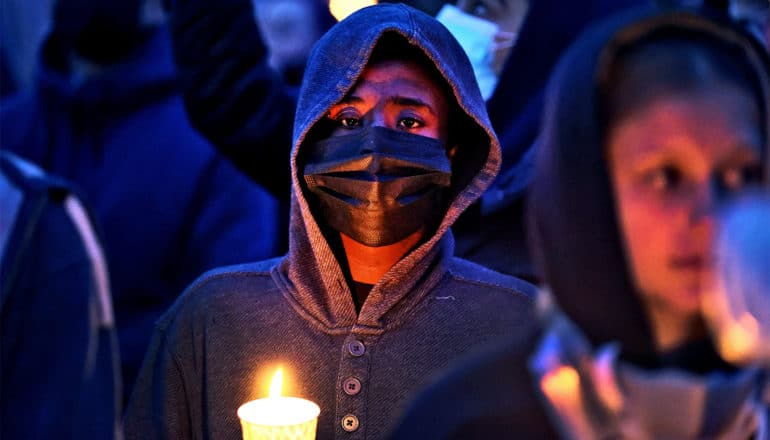 A young protester holds a candle while wearing a face mask