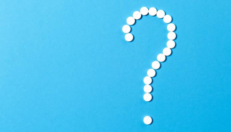 White pills in the shape of a question mark on a blue background