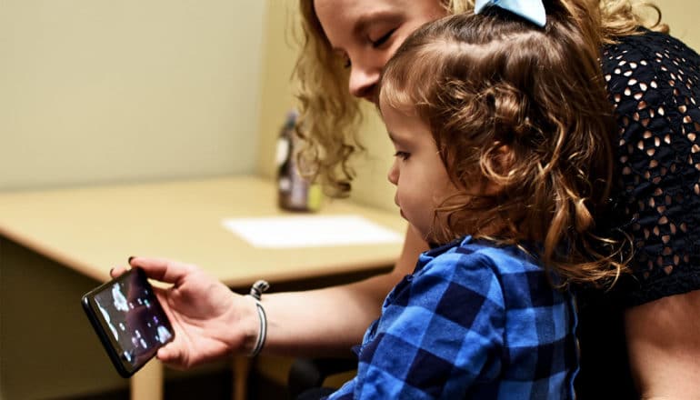 An adult holds a phone while a young girl watches the screen