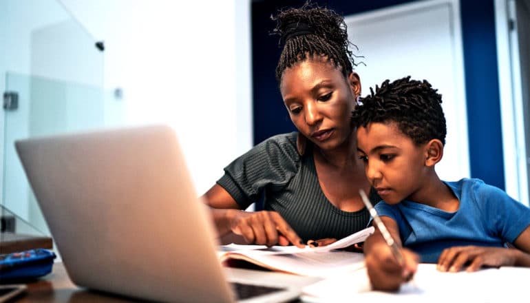 A mother helps her son with school work in front of a laptop computer