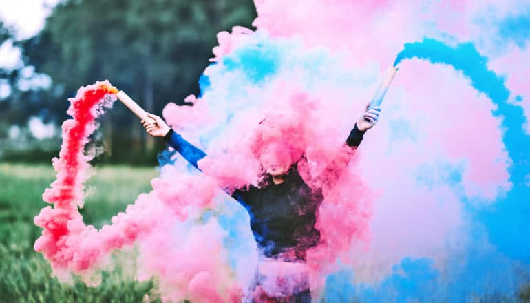 A woman holds a blue and pink flare with smoke surrounding her