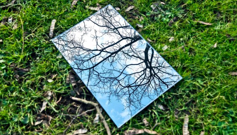 A mirror reflecting the blue sky sits on green grass