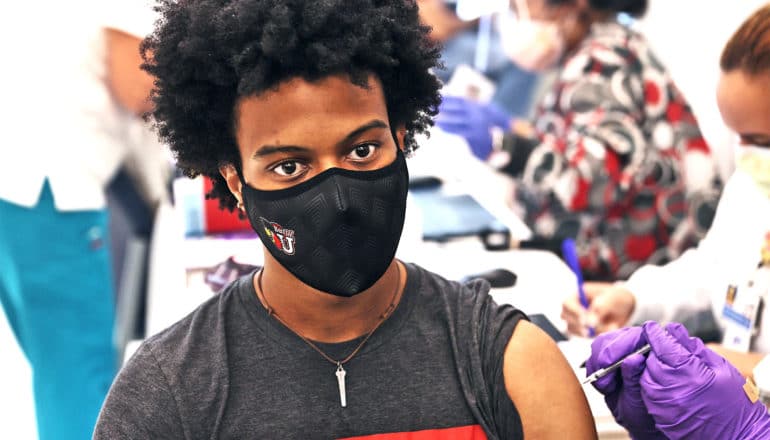 A young man wearing a face mask gets the COVID-19 vaccine