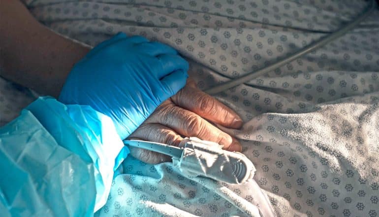 A health care worker places their blue-gloved hand over a patient's hand