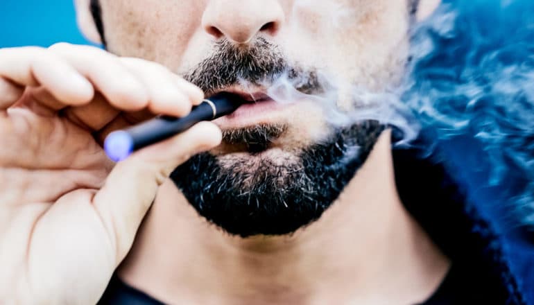 A man smokes an e-cigarette against a blue background