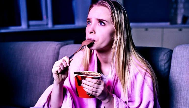 A young woman eats ice cream while watching TV