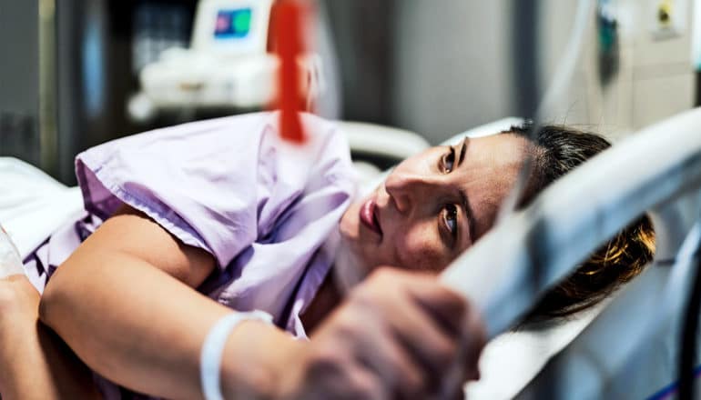 A woman about to give birth lays on a hospital bed holding the railing