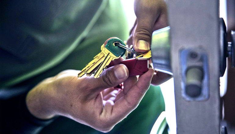 A close up of hands working on a lock while holding a ring of keys