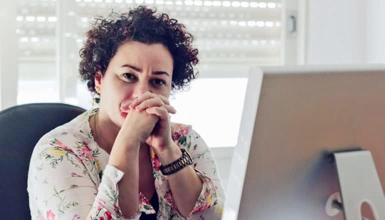 concerned adult with curly hair and floral top at computer