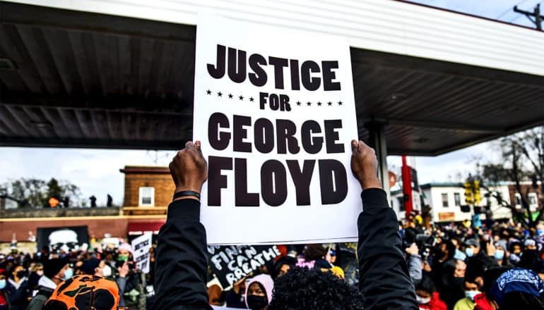 A person holds a sign that reads "Justice for George Floyd" while in a crowd of people