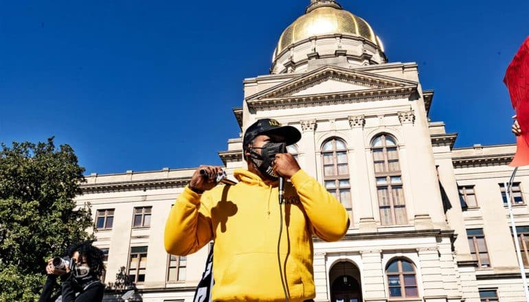 A man in a yellow hoodie speaks into a microphone outside the Georgia Capitol building