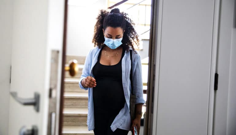 pregnant Black person wearing mask in doorway