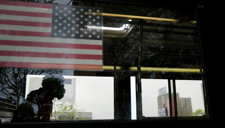 man in silhouette behind window with backward-facing US flag