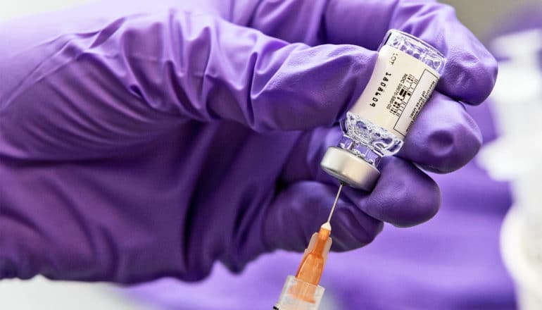 A researcher wearing a purple glove draws some Johnson & Johnson vaccine from a vial