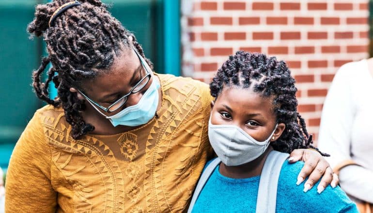 A mother comforts her daughter, who are both wearing face masks, as they walk into school