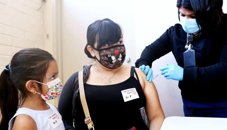 A woman gets her covid-19 vaccine while her daughter watches