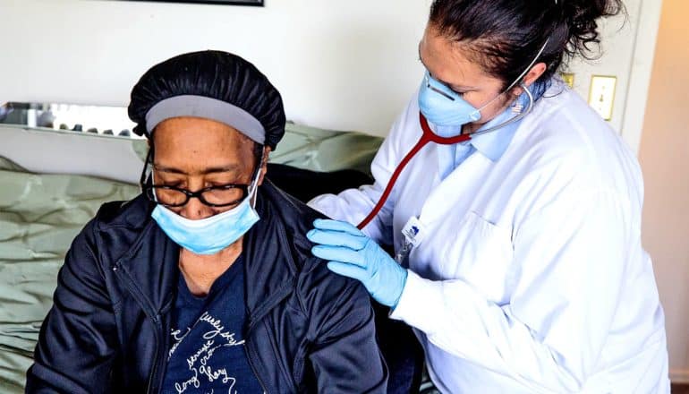 A doctor checks a patient's breathing as they sit on a bed