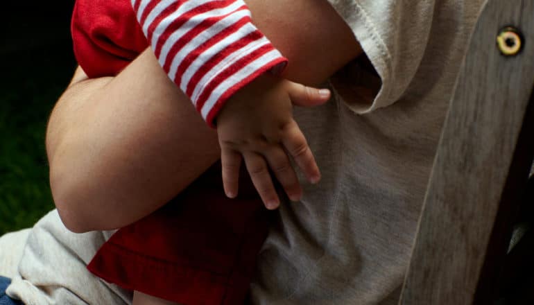 hand of baby in red/white striped top being held by unseen adult