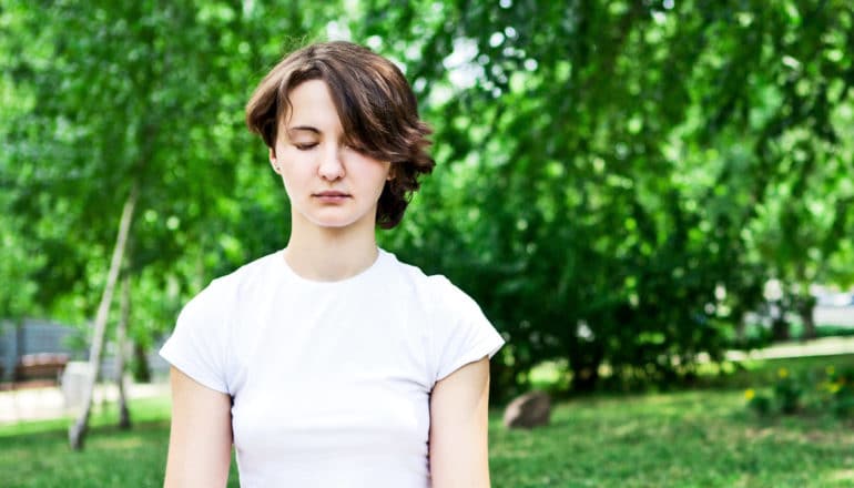 A young woman meditates in a green park