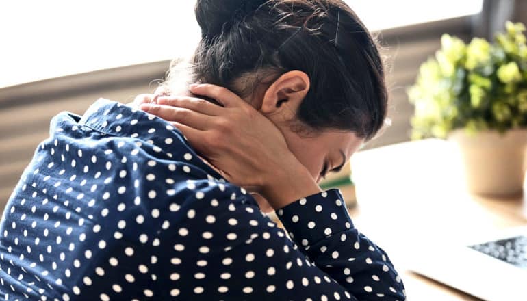 A woman at work holds the back of her neck while leaning down