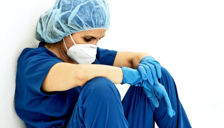 A nurse sits and leans against a wall looking down