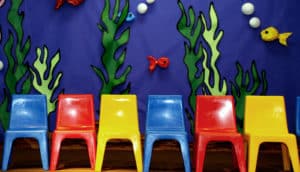 Blue, red, and yellow plastic chairs on stage in front of an ocean-themed background made of paper