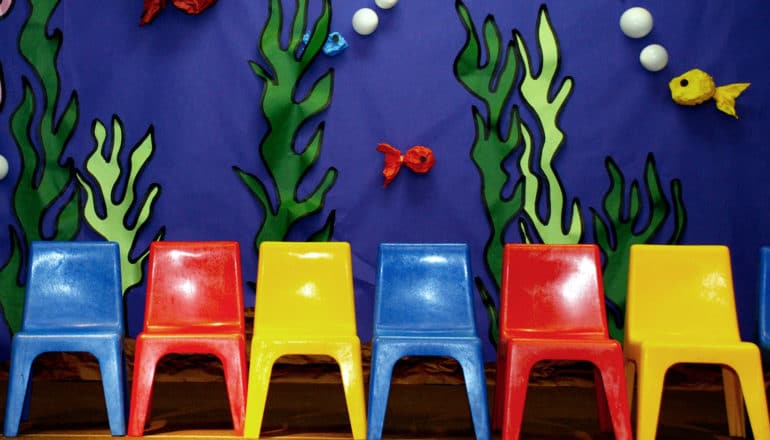 Blue, red, and yellow plastic chairs on stage in front of an ocean-themed background made of paper