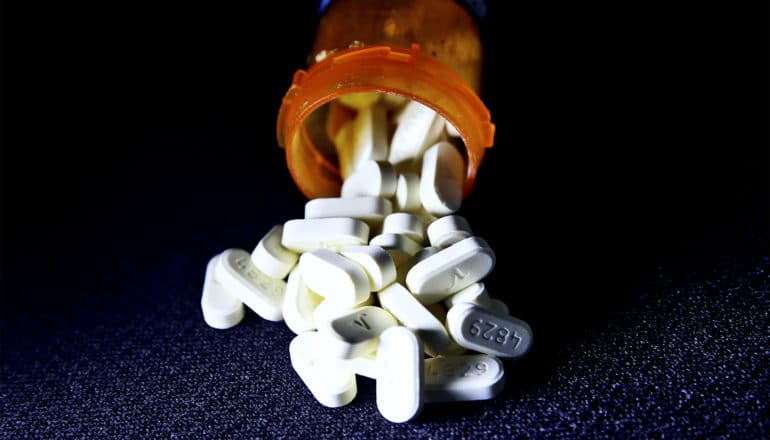 An orange pill bottle with white pills spilling out