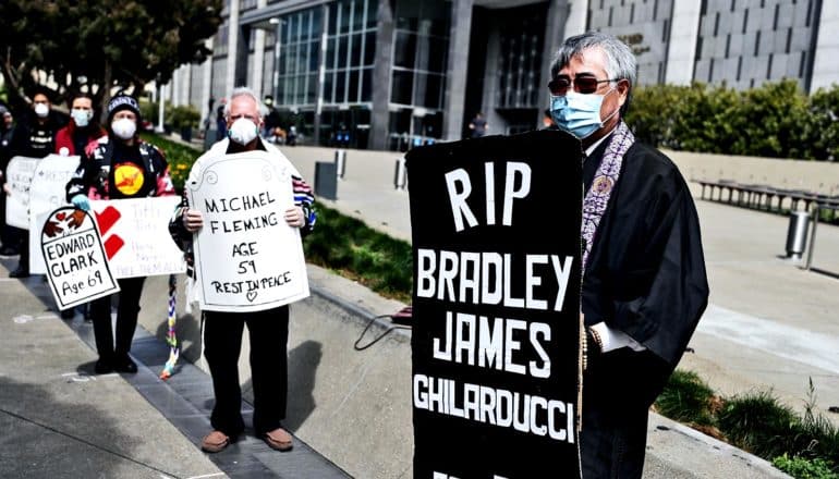 People hold signs shaped like tombstones memorializing people who died of COVID-19 in prison