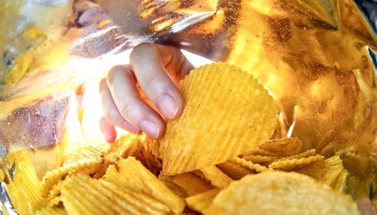 A hand reaches into a potato chip bag