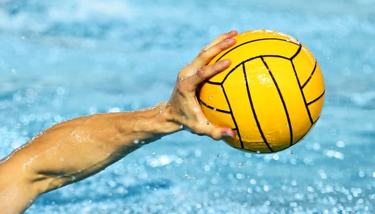 hand of person in pool grips yellow ball