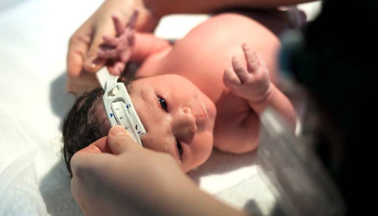 adult hands hold measuring tape around newborn head